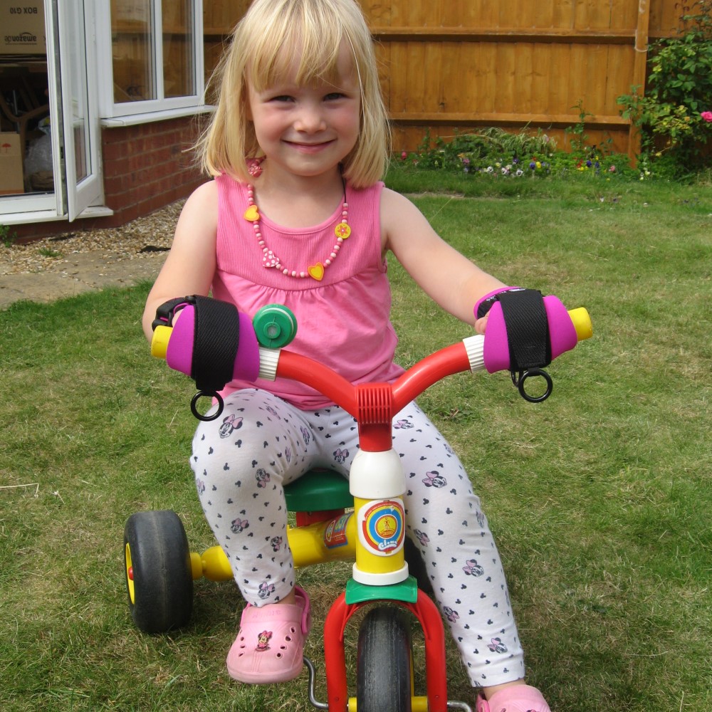 Mini gripping aid for children. girl using mini to hold onto trike. Suitable for reduced hand function: tetra, quad, cerebral palsy, SCI, spinal cord injury, stroke and more.