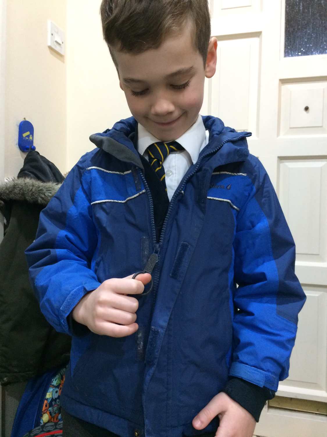 Child zips up coat using a ZipGrip with his thumb through the large loop