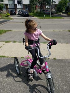 Girl on trike using gripping aids. Adaptive gym equipment. Suitable for reduced hand function: tetra, quad, cerebral palsy, SCI, spinal cord injury, limb difference, stroke and more.