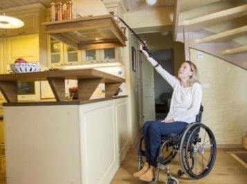 Reacher/ grabber for quadriplegics being used by woman in wheelchair to reach high shelf