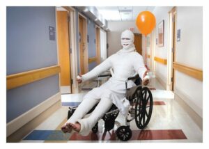 person in wheelchair with bandages covering entire body, holding a balloon