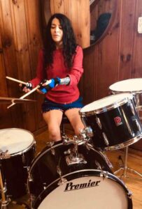 lady playing the drums using the small item gripping aid to hold her drumsticks