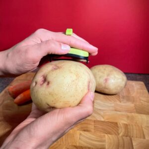 Green palm peeler being used to peel a potato