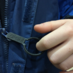 a child holding a zip grip to undo their blue raincoat. Make unzipping with poor hand function easy