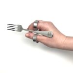 A hand holding the cutlery with loops fork. The loops sit around your finger and thumb.