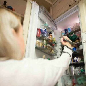 the reacher/grabber is being used to get something off the top shelf of a fridge by a female in a wheelchair