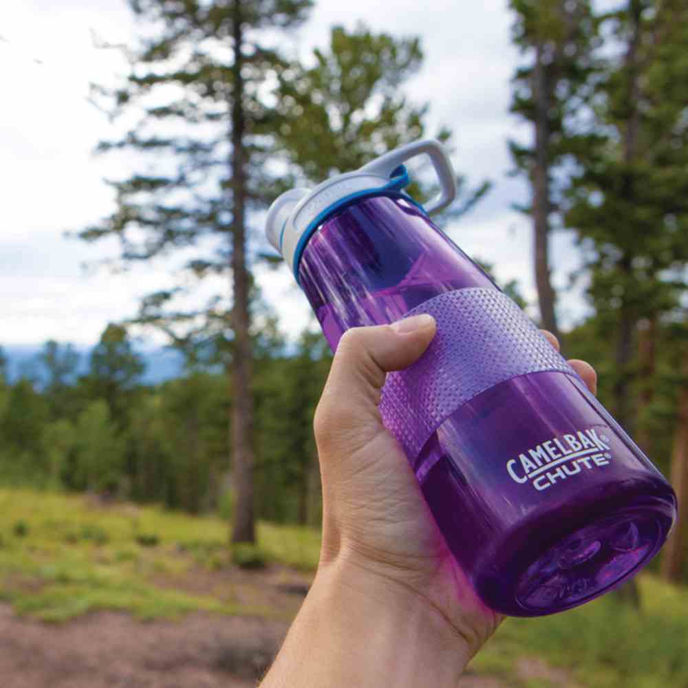 a purple water bottle with clear Cat Tongue grip on it being held aloft by a hand