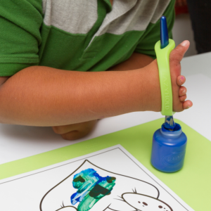 A child with a limb difference uses a green EazyHold to hold a paintbrush