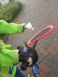 Hand holding a child's badminton racket using our general purpose gripping aid. The other hand is poised ready to serve the shuttlecock.