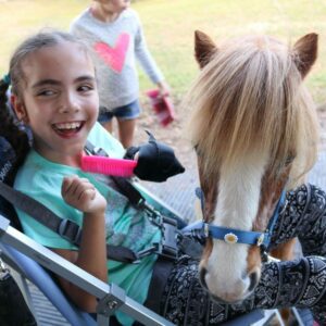 Alyssa smiling holding a brush with her General Purpose aid, brushing a pony