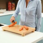 a woman uses the food prep board to hold a carrot still while she peels it