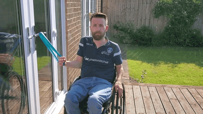 a gif of Gareth doing an internal rotation exercise with a theraband while sat outside enjoying the sunshine