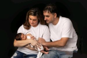 A couple in white t-shirts and jeans cuddle a newborn baby