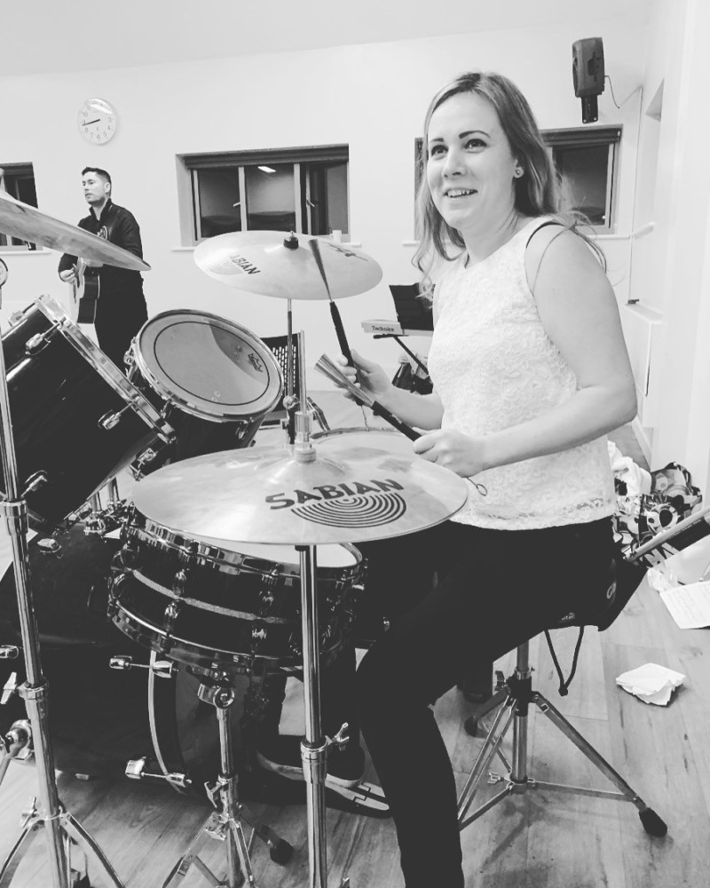 Sarah smiling whilst playing the drums