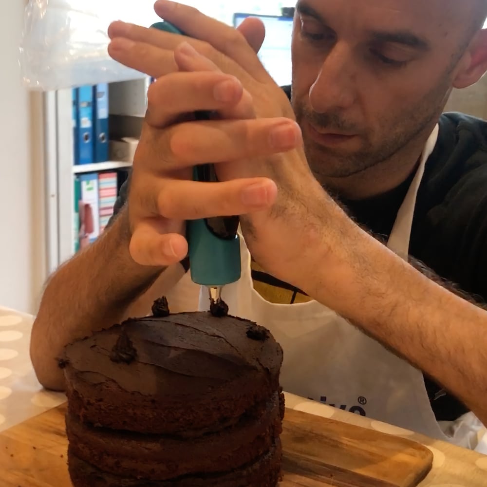 Rob uses the icing pen with two hands to decorate a chocolate cake
