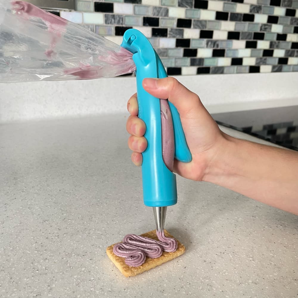 icing pen being used with one hand to pipe purple icing on to a biscuit using the star nozzle
