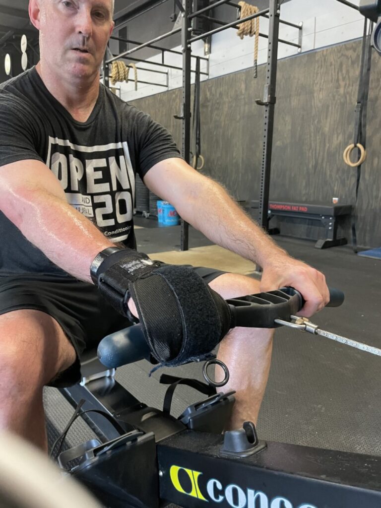 Paul uses his General Purpose aid to hold a rowing machine handle with his stroke-affected right hand