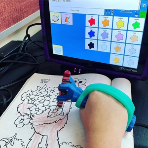 function hand used for colouring, with EazyHold strap over hand to help with grip, with communication aid directing colours
