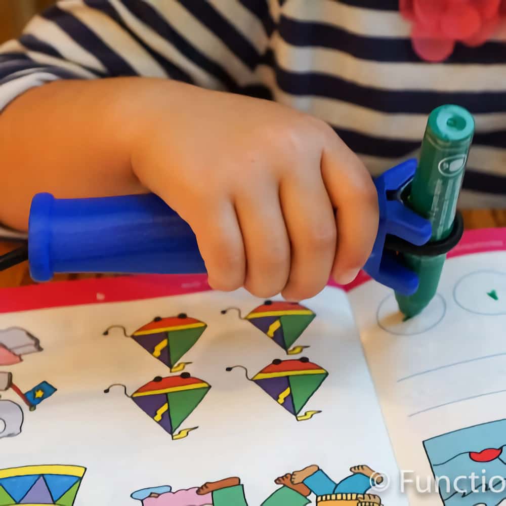 A child uses the Functional hand to hold a felt tip pen while making marks in a workbook.