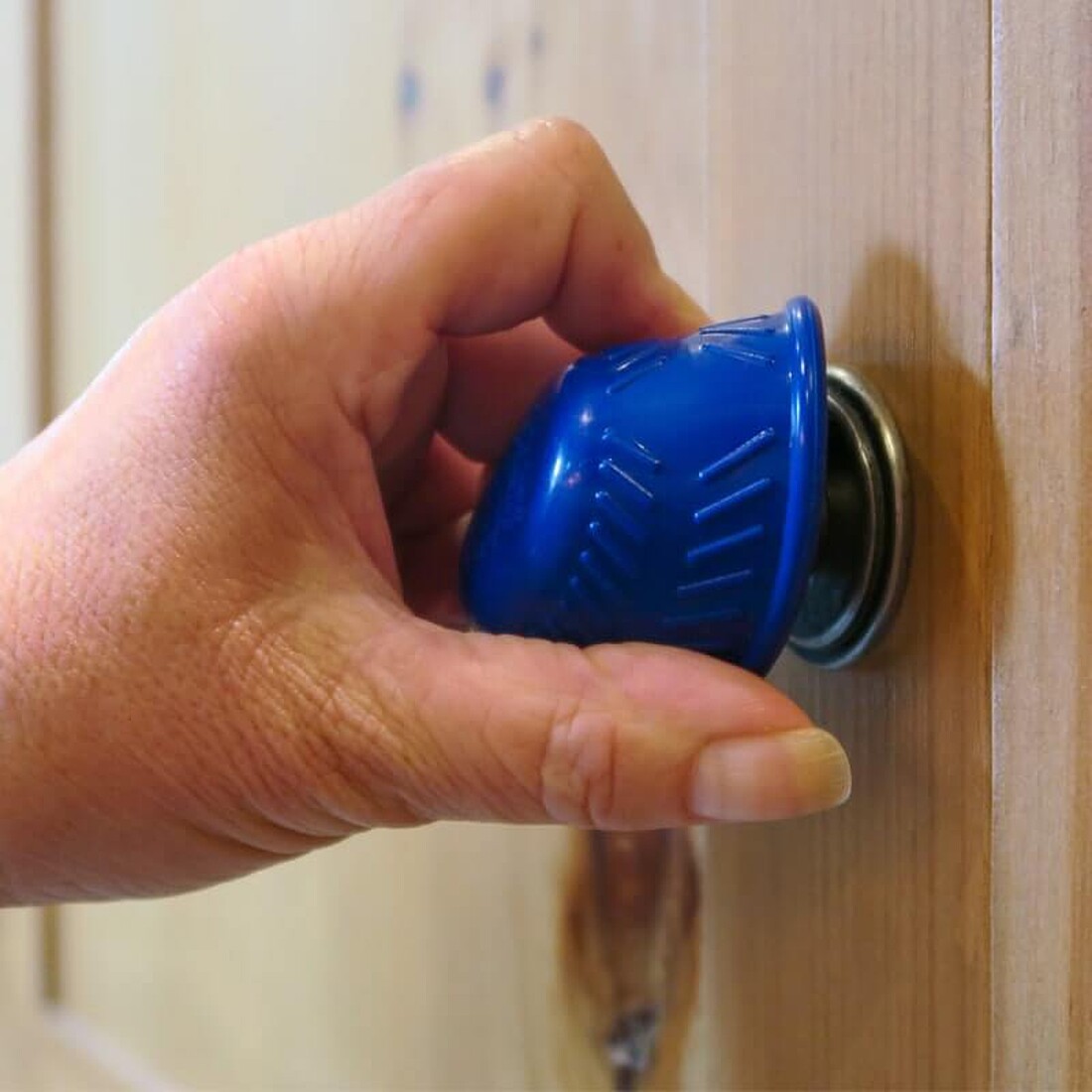 A blue silicone bottle opener being used to open a door handle
