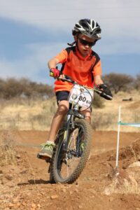 Image shows child riding a bike on a race track, using Active Hands gripping aid to support him in holding the handle bars
