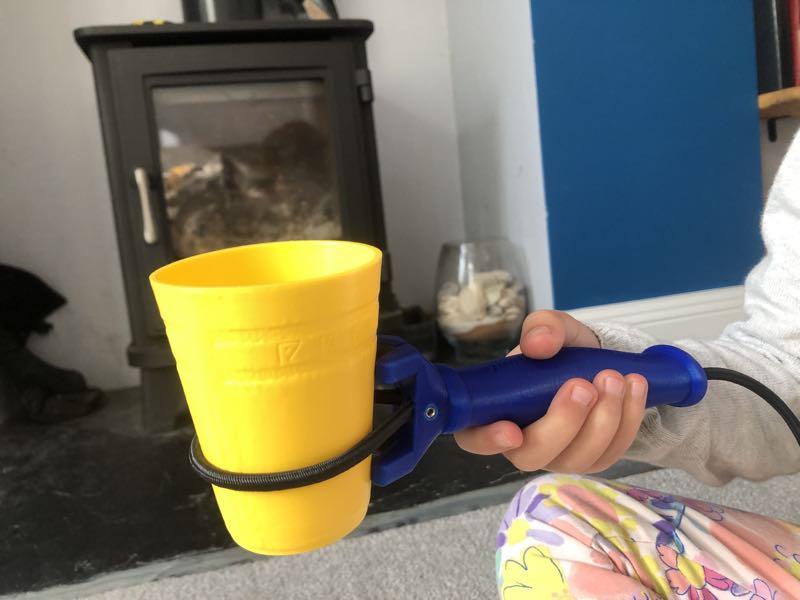Image shows a child's hand holding the functional hand product which is gripping a yellow dice cup.