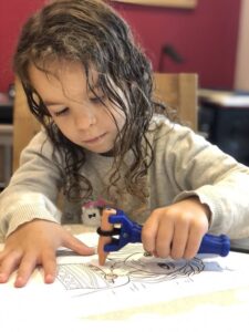 Child uses functional hand product to grip a crayon and colour in a picture.