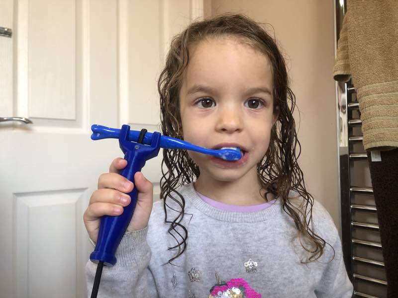 Child uses functional hand product to hold a toothbrush and brush her teeth.