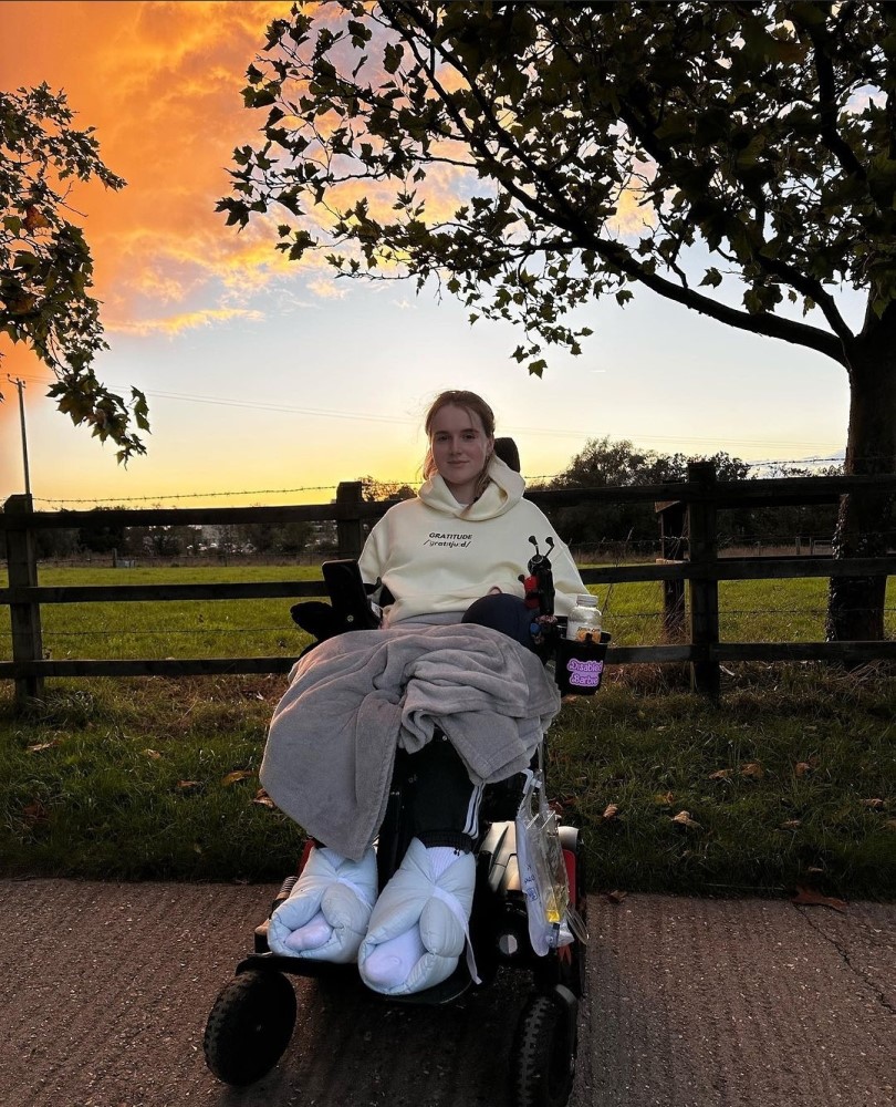 Georgia Carmichael smiling in her power chair in front of a sunset