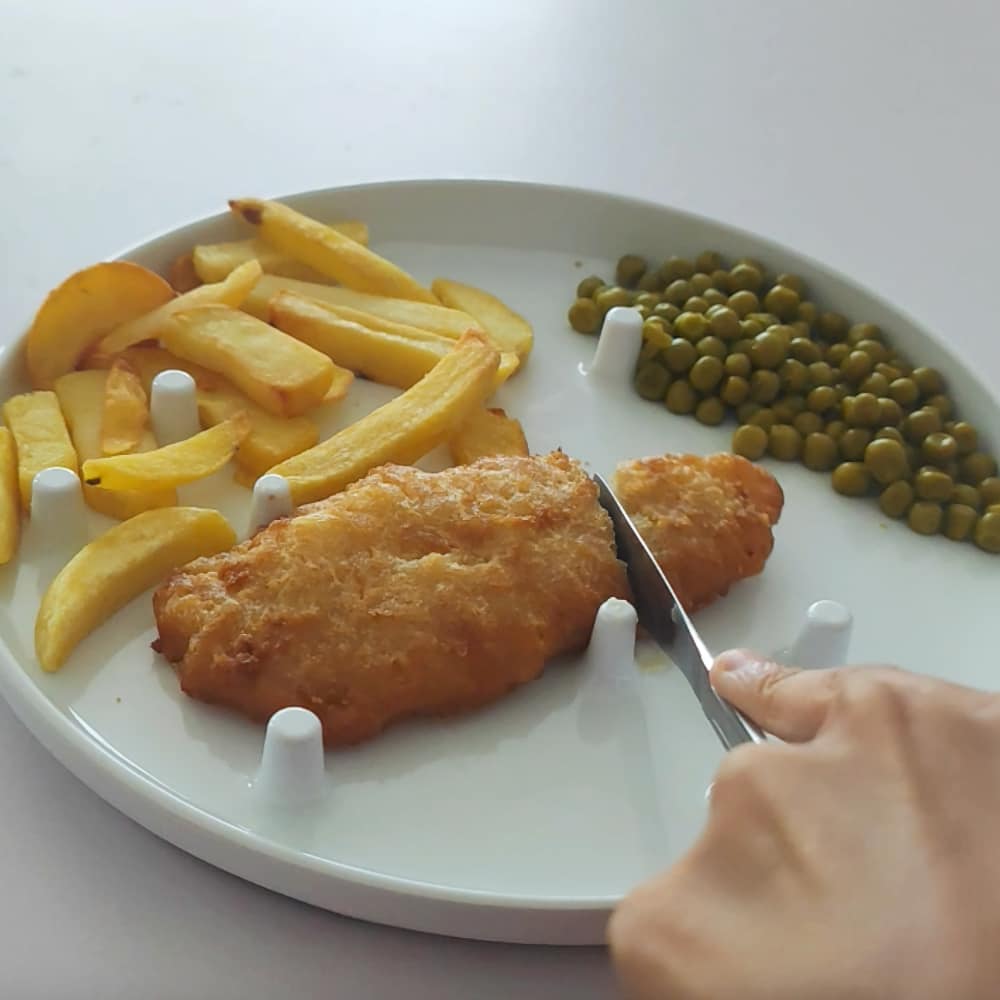 Hannah uses the one-handed plate to hold fish in place while she cuts it and to scoop peas against the lip.