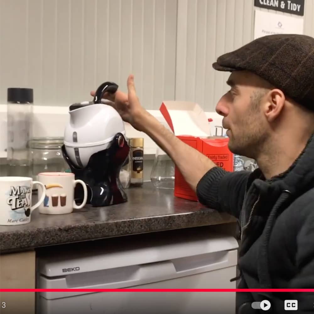 A man with reduced hand function is making tea. He is pouring water from a kettle which he is just tipping in a base in which it pivots. No need for him to lift a heavy, hot kettle.