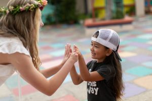 An older girl gives a high-five to a younger girl. Both have limb difference in their hands.