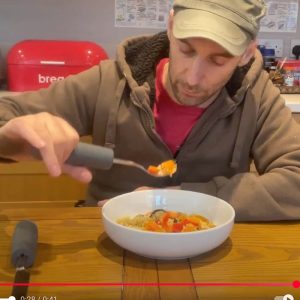 Image shows a man eating with a fork. The fork has the addition of a chunky cutlery grip added to its handle. This makes it easier to hold with reduced grip.