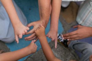 The image shows six different hands all placed into the middle of a circle. Each hand shows limb difference. The photo is a celebration of each individual.