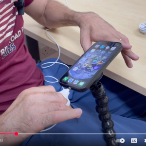 image shows a close up of someone plugging the charger into their iPhone using a cable puller device with two finger loops to support reduced finger function.