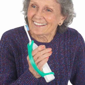 Image shows an older lady holding an electric toothbrush with a green eazyhold strap on it, to support her grip. She is smiling.