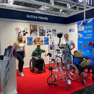 Image shows the active hands exhibition stand set up before customers arrive. Rob, millie and Jo pose and smile in the stand.