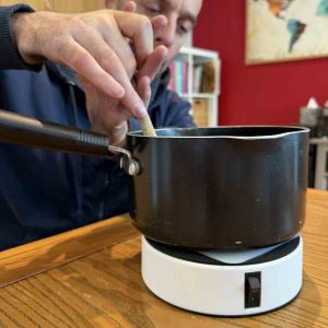 image shows a saucepan on the hold fast platform. Rob is using a wooden spoon to stir the contents.